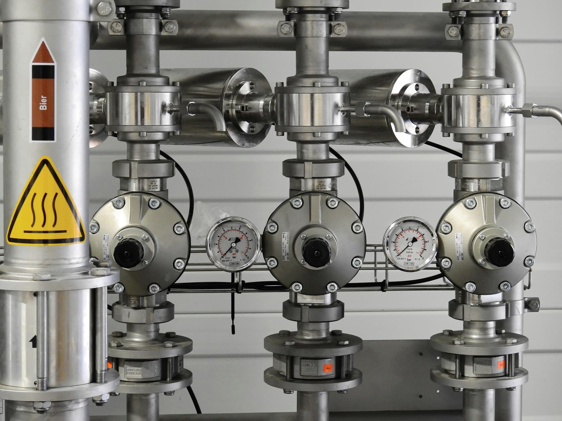 Stainless steel industrial piping with valves and pressure gauges — precision fluid handling systems used with positive displacement pumps