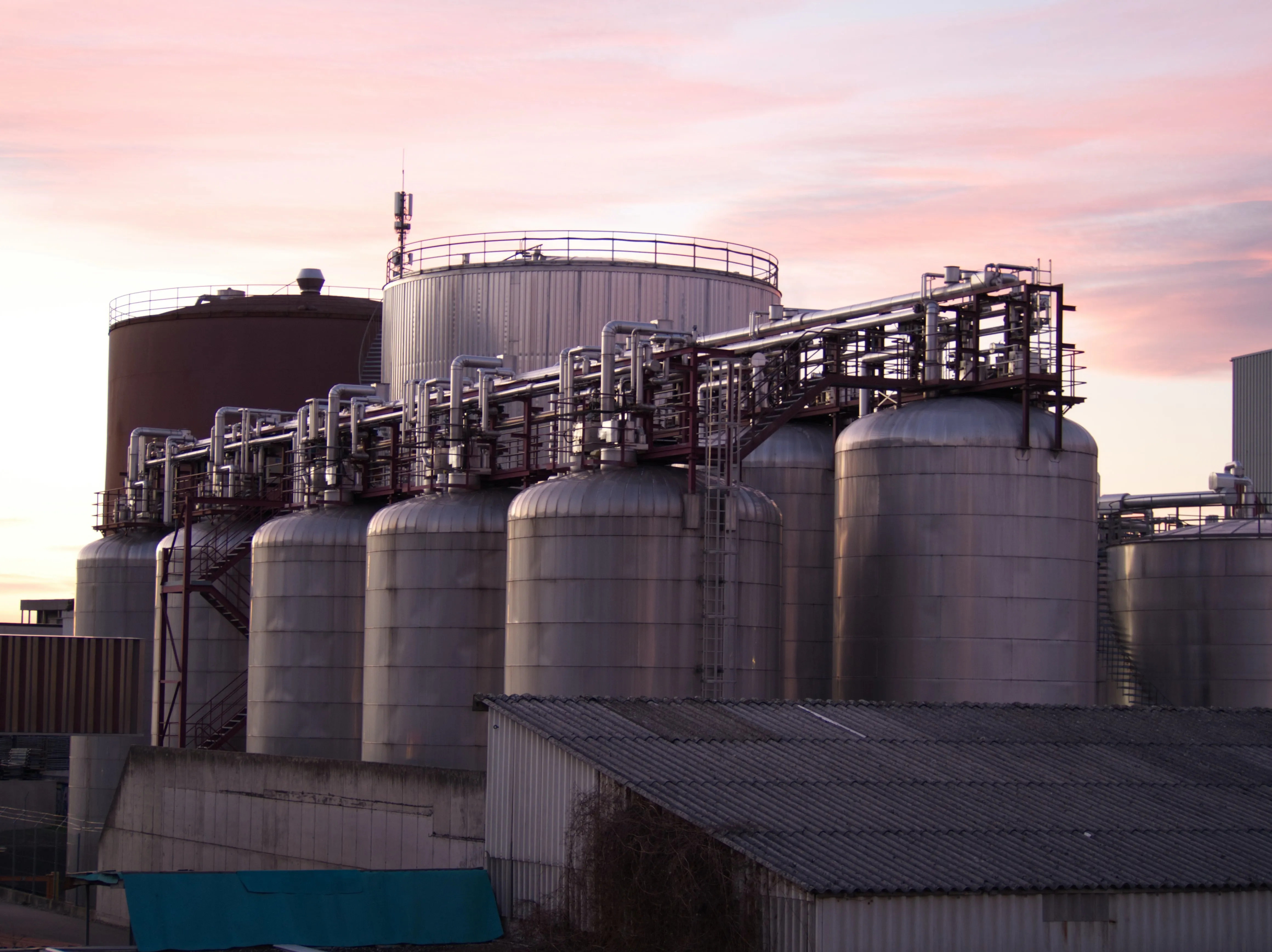 Stainless steel industrial storage tanks with interconnected piping at a processing facility